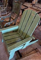 Green wooden Adirondack chair front, rocking chair visible behind