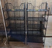 Front view of both black metal shelving units showing four adjustable lattice shelves each