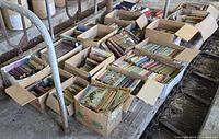 Multiple open boxes filled with assorted books and comics on concrete platform