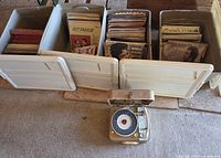 Overview of three storage totes filled with vinyl records and RCA Victor record player on floor