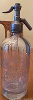 Full view of the antique glass mineral water jug showing embossed glass and metal top with lever and spout.