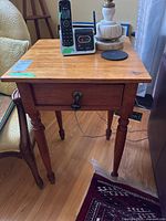 Front view of antique pine side table showing drawer and turned legs with items on top.