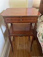 Full view of antique side table showing inlaid wood top, drawer, shelf, and slender legs with metal feet caps.