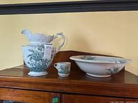 Full view of antique wash basin set showing pitcher, basin, and shave cup on wooden surface against yellow wall