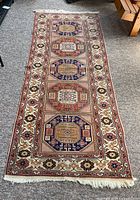 Full view of the long rectangular Armenian Kazak rug laid flat on gray carpet, showing five octagonal medallions and detailed border.