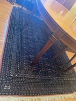 Full view of the dark blue and pink Bokhara patterned wool rug beneath a wooden dining table and floral upholstered chairs showing overall condition and pattern.