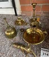 Set of brass decorative items including four candle holders, brass plant mister, and bottle opener displayed on a carpeted surface.