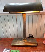 Front view of brass desk lamp on wooden surface with pull chain extended, showing overall design