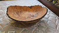 Shallow live-edge wood bowl shown from side angle displaying bark rim and interior grain