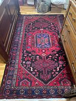 Full view of Tuisserkan rug showing central medallion and red field with geometric patterns on wood floor between furniture.