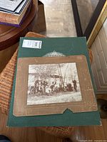 Photo of the antique sepia tone photo mounted on cardboard laid atop the green hardcover historical atlas.