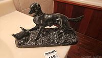 Side view of cast iron hunting dog sculpture, showing dog in pointing stance over grouse on textured base.