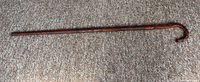 Full length view of the walking stick, showing its slim tapered shape and curved handle wrapped in patterned hide.
