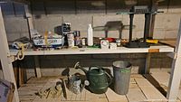 Wide view showing shelf with paint containers, timers, phone, desk lamp, watering cans, and galvanized pails below.