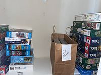 Wider view showing stacks of puzzle boxes and a paper bag labeled '24 Puzzles' with two Cobble Hill puzzle boxes clearly visible inside.
