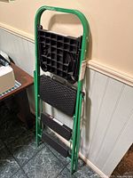 Side view of folded green metal step ladder showing three black textured steps and a handle.