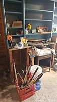 General overview of tools and crates on work tables including hand saws, gardening shears and a red crate of assorted hand tools