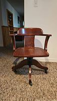 Front view of the vintage wood desk chair with curved armrests and backrest, sitting on a carpeted floor.
