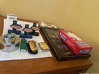 Full lot view showing the three Las Vegas souvenir lighters including table lighters and Zippo lighter, vintage pipe lighter with pouch, Bic lighter, box of candles, bag of seashells, and wooden plaque.