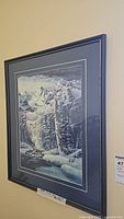 Framed watercolour painting showing snowy mountains, pine trees, and a river in a winter landscape, viewed from an angle.