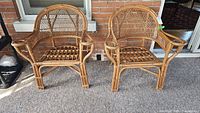 Two wicker chairs side by side in front of brick wall and window
