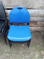 Front view of a blue plastic chair with black metal folding frame on dirt ground against weathered wooden surface.