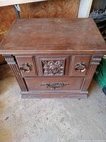 Front view of 2 drawer wooden dresser showing decorative carved detailing and metal ring handles.