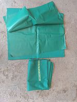 Two folded pieces of green leather on concrete floor, one piece larger and unfolded showing texture.