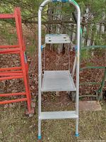 Aluminum 2 step ladder with two wide steps, plastic feet caps, showing paint splatters and outdoor wear.