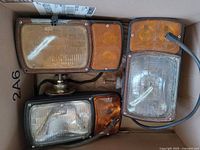 Three plow lights in cardboard box showing clear and amber lenses and metal housings with wiring.