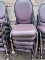 Stacked six purple padded chairs with black metal frames and armrests, showing minor wear and stacking marks.