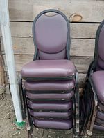 Stack of 6 purple padded chairs with black metal frames against a wooden backdrop.
