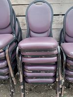 Stacked view of six purple padded chairs showing wear on black metal frames with chipped paint.