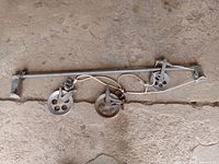 Clothesline bar laid on the ground, clearly showing three metal pulleys (rollers) and cords attached.