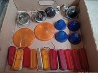 Box with various trailer lights and lenses including orange and blue round covers, red and amber rectangular lenses, and sealed beam light fixtures.