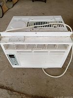 Front view of Midea window air conditioner with remote placed on top, unit shows signs of wear and dirt.