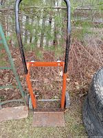 Photo of orange and black dolly cart with removable handle, showing metal frame, base plate and wheels.