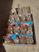 Top view of three open boxes containing empty vintage Pepsi and Coca-Cola glass bottles arranged standing up.
