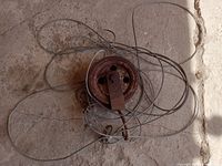 Overhead view of rusty metal pulley winch with steel cable loosely coiled around it, showing the overall size and condition.