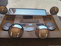 Multiple Blue Bird school bus accessories including mirrors, headlights, and metal nameplates arranged on wooden board.