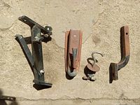 Several metal trailer parts on concrete floor including stabilizer jacks, hooks, and brackets.