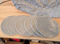 Six round cloth trivets laid out overlapping on a wooden surface with a textured gray cloth behind them.