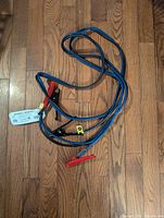 Photo of black and blue insulated booster cables with red and black clamps laid flat on a wooden floor.