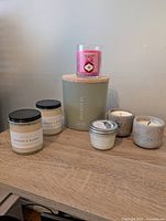 Photo showing full candle lot on a wooden surface incl. Sea & Sand large candle, Pink Berry candle, two ceramic holder candles, small silver metal jar candle and Dragon's Blood candles.