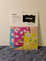 Photo of the packaged Cricut printable sticker paper with decorative stickers applied on notebooks and folders.