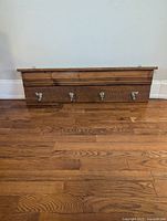 Front view of a handmade wood coat rack laid on the floor showing four metal hooks and wood grain finish.