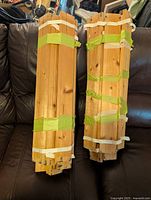 Two bundles of wooden slats bundled together with green and white straps placed on a dark leather couch.