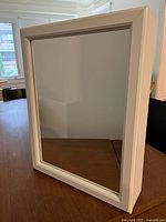 Medicine cabinet front view showing framed mirror door in white.