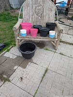 Photo of six assorted plastic outdoor planters and two small ceramic indoor planters placed on a wooden bench and ground outdoors.