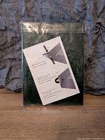 Folded dark green tarp in plastic packaging with instruction sheet showing folding and fastening steps